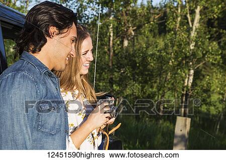 Young couple with camera standing outside their vehicle; Edmonton, Alberta, Canada View Large Photo Image Stock Photograph - Young couple with camera standing outside their vehicle; Edmonton, Alberta, Canada. Fotosearch