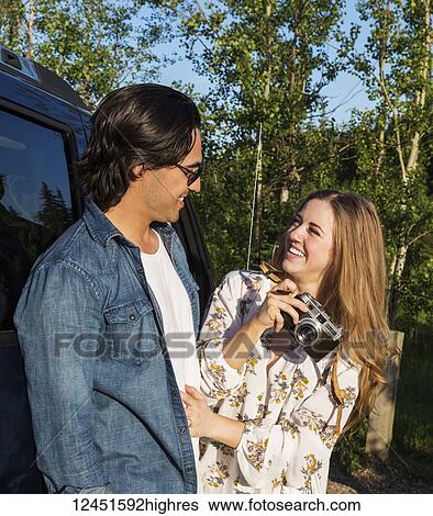 Stock Photograph - Young couple with camera standing outside their vehicle; Edmonton, Alberta, Canada. Fotosearch