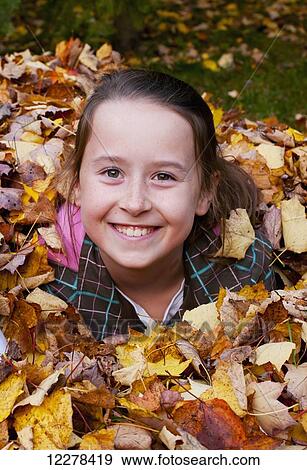 Stock Photo - Young girl playing in the fallen leaves in autumn; Knowlton, Quebec, Canada. Fotosearch