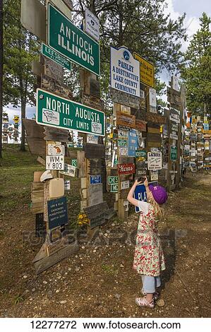 Stock Image - Young girl takes a picture with a smart phone of the Signpost Forest, Watson Lake, Yukon Territory, Canada, Summer. Fotosearch