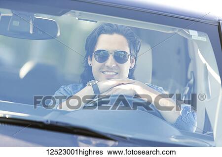 Stock Photograph - Young man sitting in the driver's seat of a vehicle posing for a picture while looking out the windshield; Edmonton, Alberta, Canada. Fotosearch