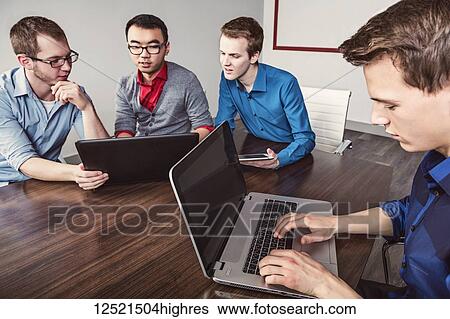 Stock Photograph - Young men who are millennial business professionals working together in a conference room in a high tech modern business; Sherwood Park, Alberta, Canada. Fotosearch