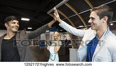 Stock Photograph - Young millennial business co-workers celebrating a success with a high-five in the workplace; Sherwood Park, Alberta, Canada. Fotosearch