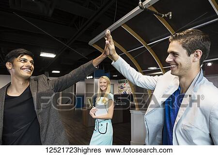 Stock Photograph - Young millennial business co-workers celebrating a success with a high-five in the workplace; Sherwood Park, Alberta, Canada. Fotosearch