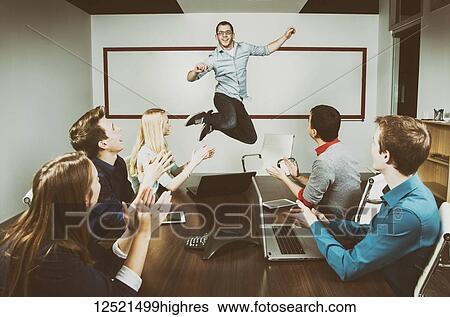 Young millennial business professional jumping to celebrate an accomplishment with his co-workers working in a conference room during a presentation and one of his piers taking a picture with a pad; Sherwood Park, Alberta, Canada View Large Photo Image Stock Photograph - Young millennial business professional jumping to celebrate an accomplishment with his co-workers working in a conference room during a presentation and one of his piers taking a picture with a pad; Sherwood Park, Alberta, Canada. Fotosearch