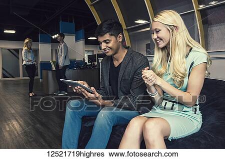 Stock Photograph - Young millennial business professionals in the workplace collaborating and using technology; Sherwood Park, Alberta, Canada. Fotosearch