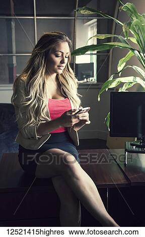 Stock Photograph - Young millennial business woman in her workplace using a smart phone; Sherwood Park, Alberta, Canada. Fotosearch