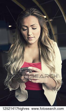Stock Photograph - Young millennial business woman in her workplace using a smart phone; Sherwood Park, Alberta, Canada. Fotosearch