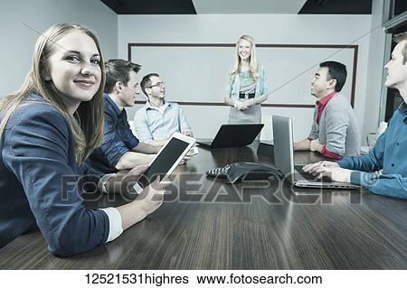 Young millennial business woman looking at the camera while another woman is giving a presentation in a conference room in a modern place of business; Sherwood Park, Alberta, Canada View Large Photo Image Stock Photograph - Young millennial business woman looking at the camera while another woman is giving a presentation in a conference room in a modern place of business; Sherwood Park, Alberta, Canada. Fotosearch