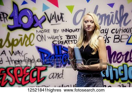 Stock Photograph - Young millennial business woman with her tablet standing against a colourful wall with motivational business graffiti; Sherwood Park, Alberta, Canada. Fotosearch