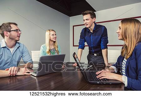 Stock Photograph - Young millennial businessman speaking to a group of young professionals in a conference room in a place of business; Sherwood Park, Alberta, Canada. Fotosearch