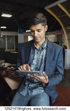 Stock Photograph - Young millennial businessman using his technology in the workplace; Sherwood Park, Alberta, Canada. Fotosearch