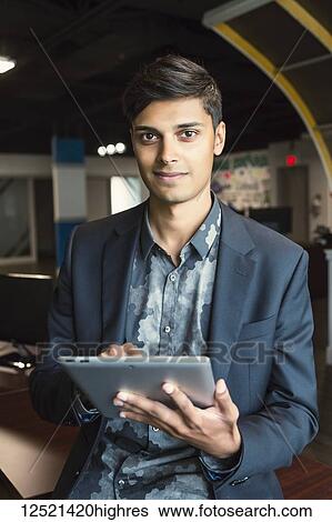 Stock Photograph - Young millennial businessman using his technology in the workplace; Sherwood Park, Alberta, Canada. Fotosearch