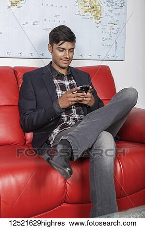 Stock Photograph - Young millennial businessman using his smart phone in the lobby of a workplace; Sherwood Park, Alberta, Canada. Fotosearch