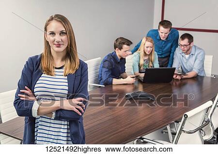 Stock Photograph - Young millennial businesswoman posing for the camera in a conference room of young professionals working together in a modern place of business; Sherwood Park, Alberta, Canada. Fotosearch