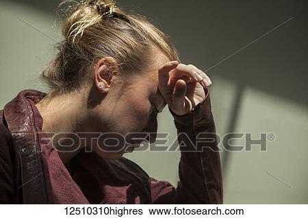 Stock Photograph - Young woman looking down and holding her head against her hand; Connecticut, United States of America. Fotosearch