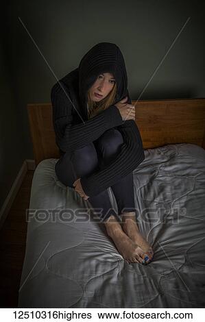 Young woman sitting on her bed wearing a hoodie with the hood up over her head, looking despondent; Connecticut, United States of America View Large Photo Image Stock Photograph - Young woman sitting on her bed wearing a hoodie with the hood up over her head, looking despondent; Connecticut, United States of America. Fotosearch