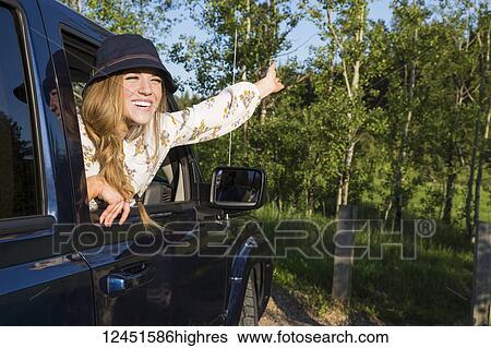 Young woman wearing hat leaning out open vehicle window with a big smile and arm raised to the sky; Edmonton, Alberta, Canada View Large Photo Image Stock Photograph - Young woman wearing hat leaning out open vehicle window with a big smile and arm raised to the sky; Edmonton, Alberta, Canada. Fotosearch