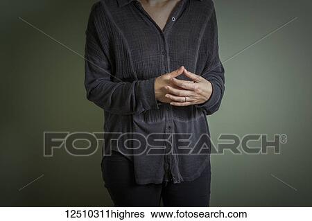 Stock Photograph - Young woman's hands held together in front of her torso as she stands against a green wall; Connecticut, United States of America. Fotosearch