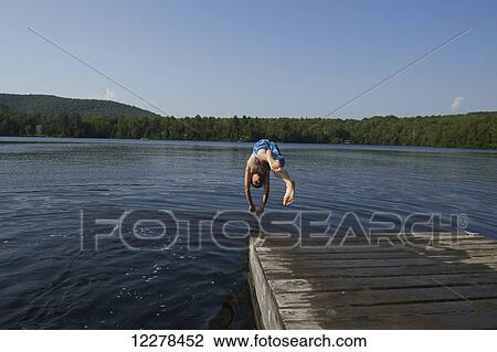 Stock Image - A boy dives into a lake from a wooden dock; Lac des Neiges, Quebec, Canada. Fotosearch