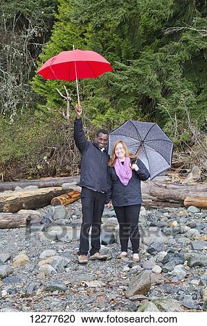 Stock Image - A couple posing with umbrellas in Whytecliff Park, Horseshoe Bay; British Columbia, Canada. Fotosearch