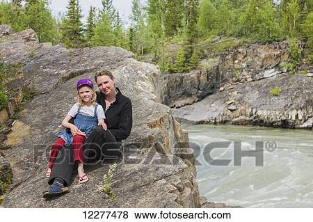 Stock Photo - A Mother and daughter sit on top of Whirlpool Canyon along the Liard River, Alaska Highway, North of Liard Hot Springs, British Columbia, Canada, Summer. Fotosearch