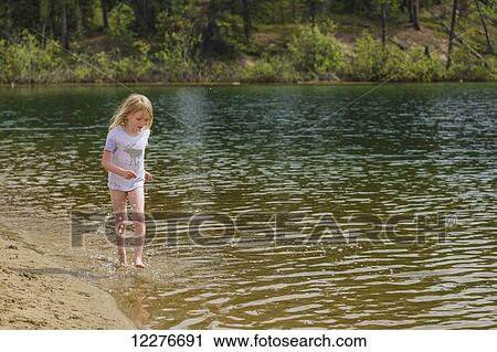 Stock Image - A young girl plays in the water along a sandy beach, Lucky Lake, Yukon Territory, Canada, Summer. Fotosearch