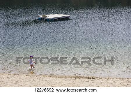 Stock Image - A young girl plays in the water along a sandy beach, Lucky Lake, Yukon Territory, Canada, Summer. Fotosearch