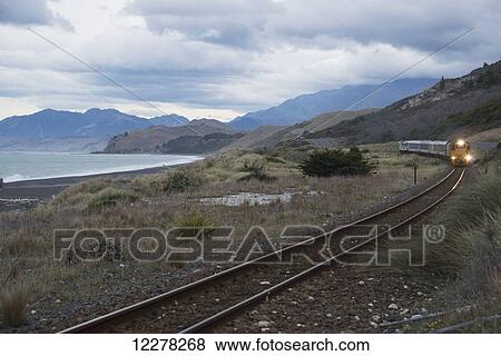 Stock Photo - Approaching train with scenic sea and mountain backdrop on East coast of New Zealand's South Island; New Zealand. Fotosearch