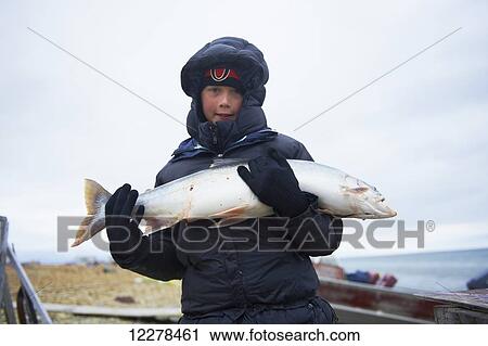 Stock Image - Boy holds fresh caught Arctic Char on the shore, near Cambridge Bay; Nunavut, Canada. Fotosearch