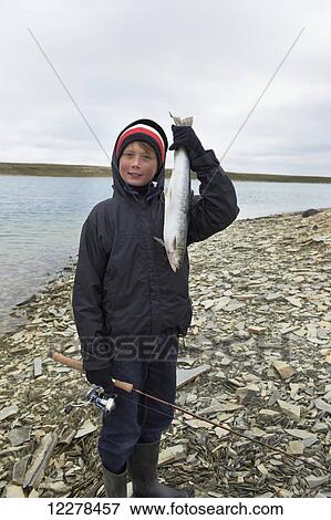 Stock Photo - Boy holds fresh caught Arctic Char while shore fishing in the Arctic Ocean, Western Arm, near Cambridge Bay; Nunavut, Canada. Fotosearch