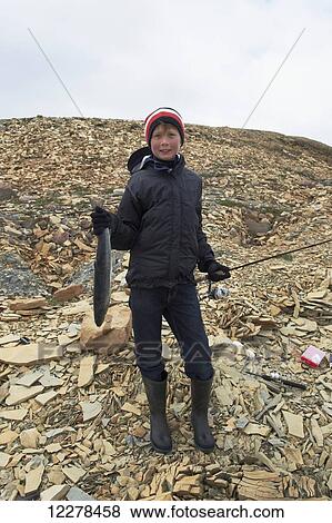 Stock Photo - Boy holds fresh caught Arctic Char while shore fishing in the Arctic Ocean, Western Arm, near Cambridge Bay; Nunavut, Canada. Fotosearch