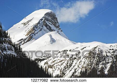 Stock Image - Close up of a snow covered mountain peak with blue sky and clouds; Banff, Alberta, Canada. Fotosearch