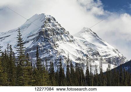 Close up of two snow covered mountain peaks with cloud cover and some blue sky; Banff, Alberta, Canada View Large Photo Image Picture - Close up of two snow covered mountain peaks with cloud cover and some blue sky; Banff, Alberta, Canada. Fotosearch