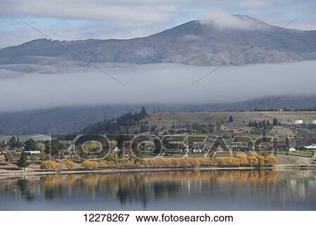 Stock Photo - Cloud straddling mountain range and Lake Ruataniwha in the foreground; Canterbury, New Zealand. Fotosearch