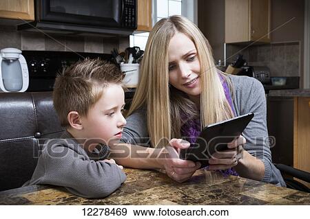Disabled mother helping her son learn on a tablet; Spruce Grove, Alberta, Canada View Large Photo Image Stock Photo - Disabled mother helping her son learn on a tablet; Spruce Grove, Alberta, Canada. Fotosearch