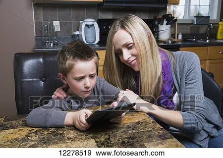 Disabled mother helping her son learn on a tablet; Spruce Grove, Alberta, Canada View Large Photo Image Stock Photo - Disabled mother helping her son learn on a tablet; Spruce Grove, Alberta, Canada. Fotosearch