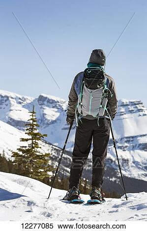 Stock Photography - Female snowshoer looking over snow covered mountain range and blue sky; Banff, Alberta, Canada. Fotosearch