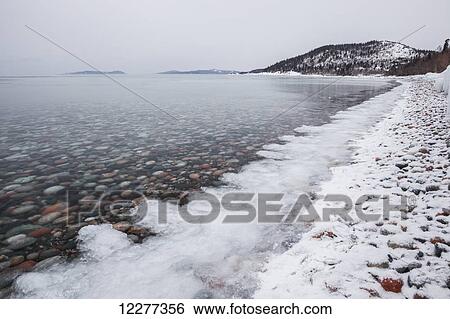 Stock Photograph - Pebbles in calm water with ice and snow along the shoreline of Lake Superior. Fotosearch