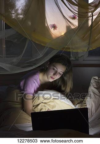 Stock Image - Teenage girl on her computer in bed; England. Fotosearch