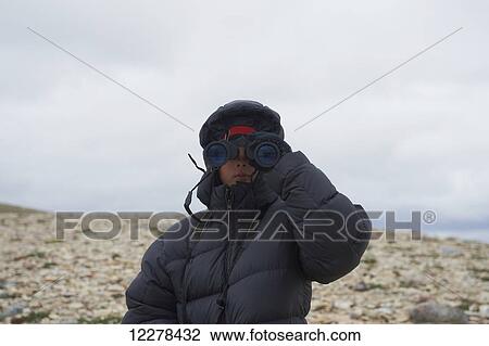 Stock Image - Teenager looking through binoculars on Mount Pelly, Ovayok Territorial Park, near Cambridge Bay; Nunavut, Canada. Fotosearch