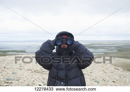 Stock Image - Teenager looking through binoculars on Mount Pelly, Ovayok Territorial Park, near Cambridge Bay; Nunavut, Canada. Fotosearch