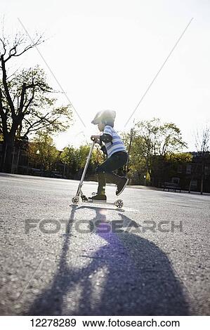 Stock Photo - Young boy riding a 2-wheeled scooter; Montreal, Quebec, Canada. Fotosearch