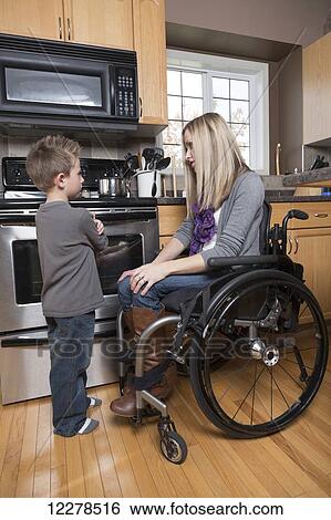 Stock Photograph - Young disabled mother talking with her young son in her kitchen; Spruce Grove, Alberta, Canada. Fotosearch