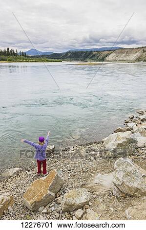 Stock Image - Young girl playing along the bank of the Yukon River, Whitehorse, Yukon Territory, Canada, Summer. Fotosearch