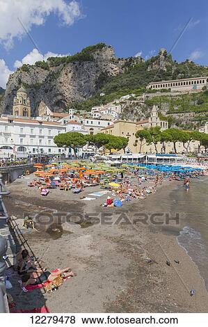 Stock Photo - A beach view of the town of Amalfi on the Amalfi Coast in Italy, with the tourists lying on the beach and the village buildings and mountains in the background; Amalfi, Province of Salerno, Italy. Fotosearch