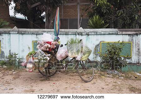 Stock Photo - A bike vegetable vendor has parked his bike against a wall, close to the local market; Kentung, Shan State, Myanmar. Fotosearch