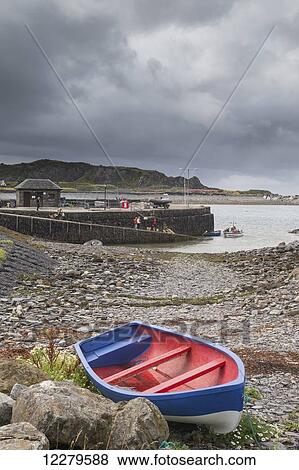 Stock Photo - A colourful rowboat on the shore with people on a boat ramp at the water's edge; Scotland. Fotosearch