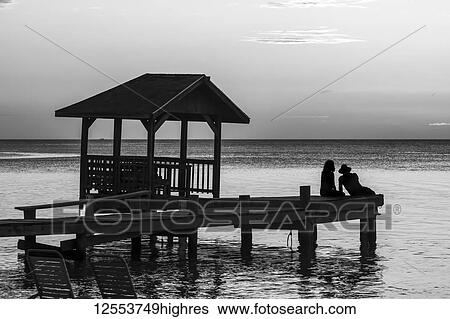 A couple sits on the end of a dock looking out to the tranquil ocean at sunset; Roatan, Bay Islands Department, Honduras View Large Photo Image Stock Photograph - A couple sits on the end of a dock looking out to the tranquil ocean at sunset; Roatan, Bay Islands Department, Honduras. Fotosearch