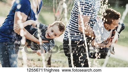 Stock Photograph - A family with young children playing at a spray park; Edmonton, Alberta, Canada. Fotosearch